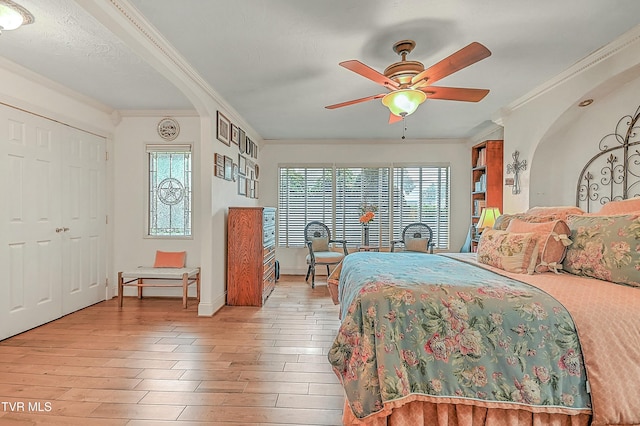 bedroom featuring light wood-type flooring, crown molding, arched walkways, and baseboards