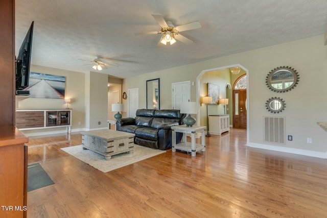 living area with visible vents, light wood-style flooring, ceiling fan, a textured ceiling, and baseboards