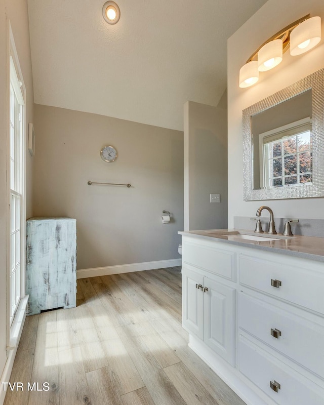 bathroom featuring baseboards, lofted ceiling, toilet, wood finished floors, and vanity