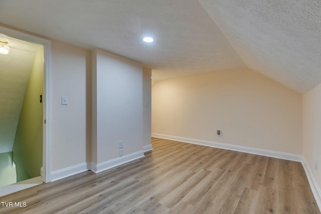 additional living space featuring light wood-style floors, vaulted ceiling, a textured ceiling, and baseboards