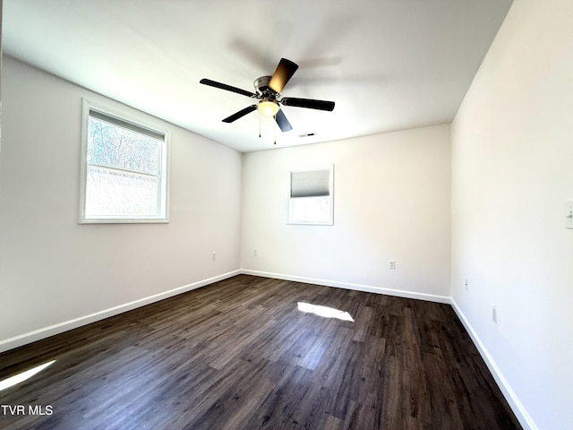 empty room with a ceiling fan, visible vents, dark wood finished floors, and baseboards