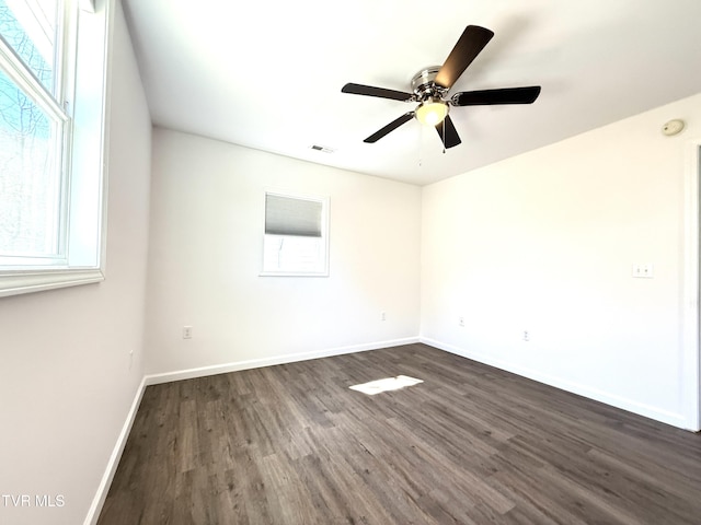 empty room featuring dark wood-style floors, a ceiling fan, visible vents, and baseboards