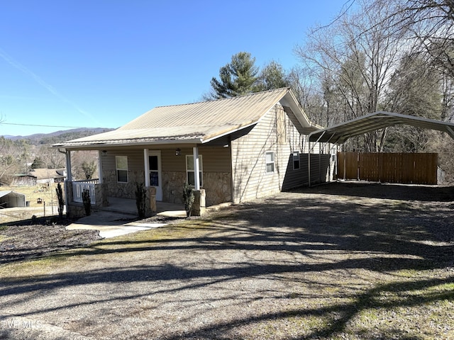 view of home's exterior featuring metal roof, covered porch, driveway, stone siding, and a detached carport