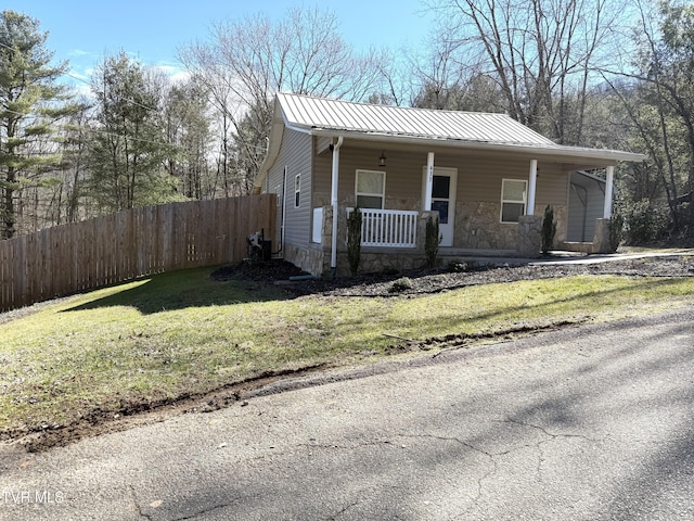 view of front facade with a porch, fence, metal roof, stone siding, and a front lawn