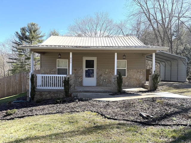 view of front facade with stone siding, metal roof, fence, a porch, and a detached carport