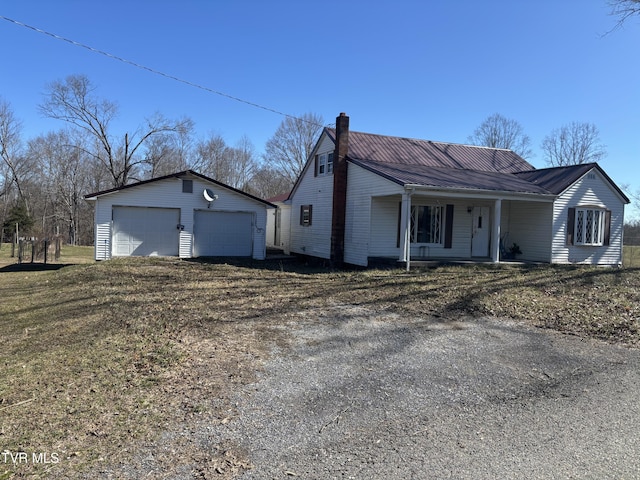 view of front of home with an outbuilding, covered porch, a chimney, a detached garage, and metal roof