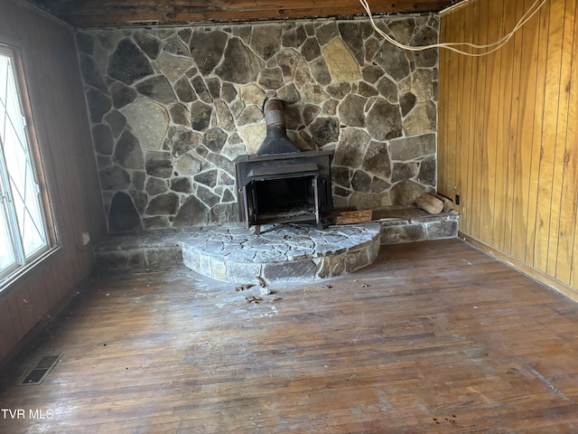 details with visible vents, wood finished floors, a wood stove, and wood walls