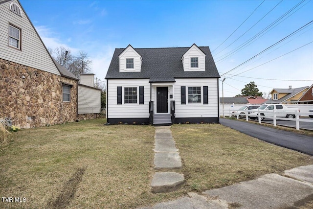 new england style home featuring roof with shingles and a front lawn