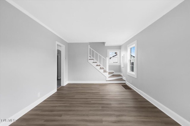 unfurnished living room featuring crown molding, dark wood finished floors, baseboards, and stairs