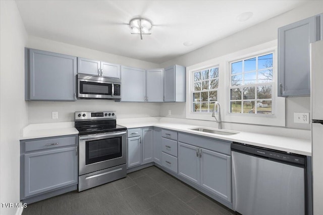 kitchen with appliances with stainless steel finishes, gray cabinets, light countertops, and a sink