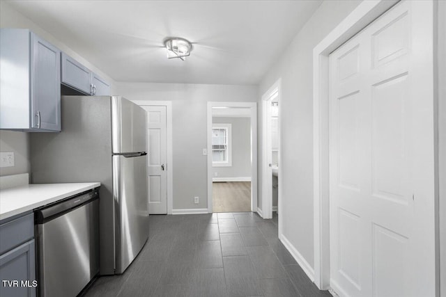 kitchen featuring baseboards, light countertops, stainless steel dishwasher, and gray cabinetry