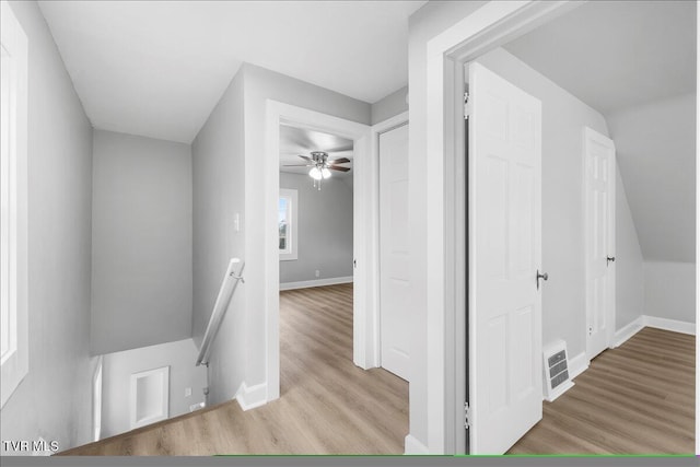 corridor with visible vents, wood finished floors, an upstairs landing, and baseboards