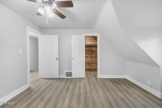 unfurnished bedroom with vaulted ceiling, baseboards, a walk in closet, and wood finished floors