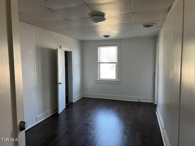 unfurnished bedroom with dark wood-type flooring, a drop ceiling, visible vents, and baseboards