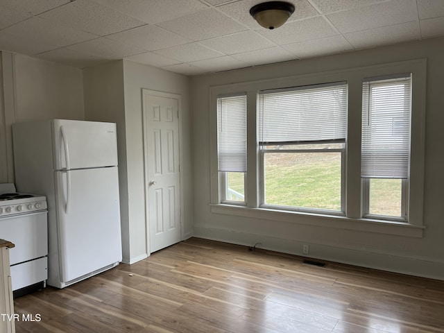 kitchen featuring white appliances, a drop ceiling, wood finished floors, and baseboards