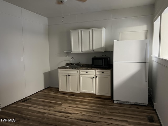 kitchen featuring dark countertops, dark wood-type flooring, freestanding refrigerator, black microwave, and a sink