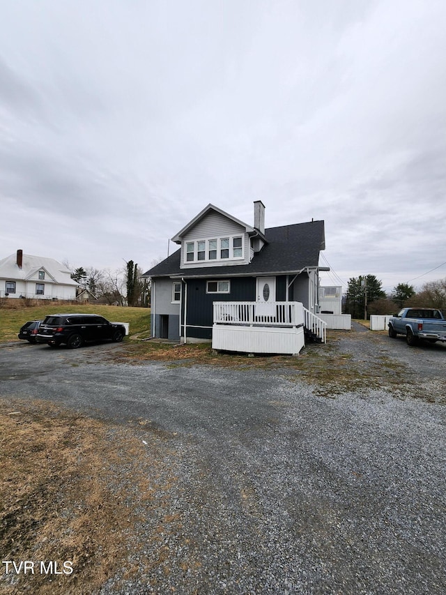 view of front facade featuring a deck, driveway, and a chimney