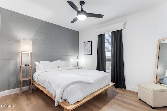 bedroom with light wood-type flooring, ceiling fan, an accent wall, and baseboards