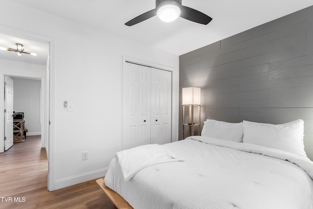 bedroom featuring light wood finished floors, wooden walls, baseboards, a ceiling fan, and a closet