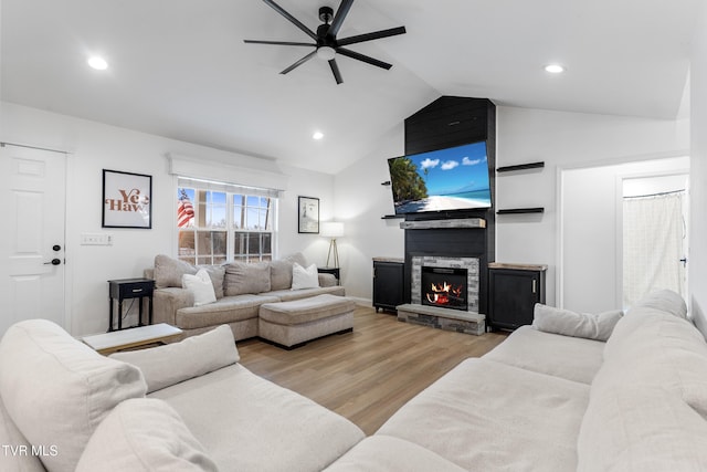 living area featuring light wood-type flooring, recessed lighting, vaulted ceiling, and a stone fireplace