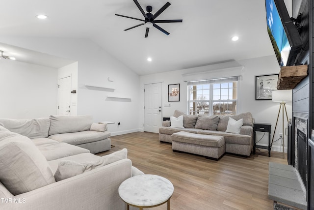 living area featuring ceiling fan, a large fireplace, baseboards, vaulted ceiling, and light wood-style floors