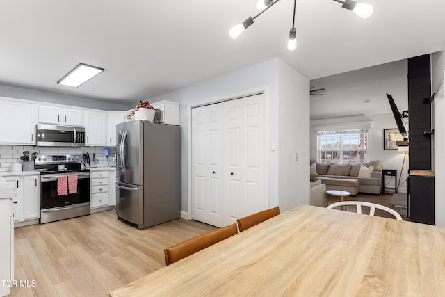 kitchen featuring white cabinetry, light countertops, appliances with stainless steel finishes, decorative backsplash, and light wood finished floors