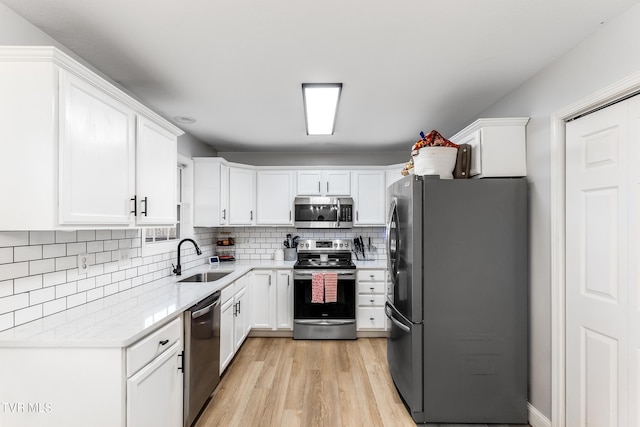 kitchen with light wood finished floors, tasteful backsplash, white cabinets, appliances with stainless steel finishes, and a sink