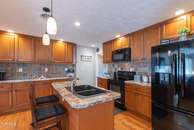 kitchen with brown cabinetry, a sink, light wood-style flooring, and black appliances