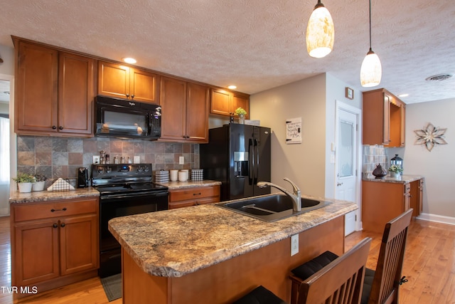 kitchen with black appliances, brown cabinetry, a sink, and light wood-style floors