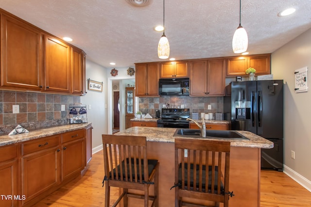 kitchen with black appliances, brown cabinetry, a sink, and light wood-style floors