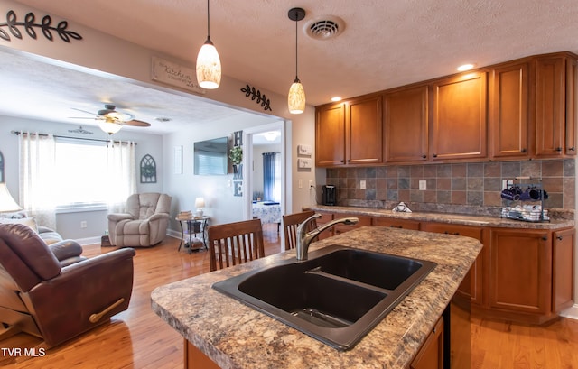 kitchen featuring brown cabinetry, visible vents, open floor plan, and a sink