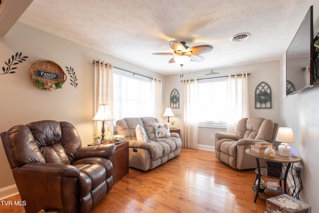living room with a textured ceiling, ceiling fan, light wood-style flooring, visible vents, and baseboards