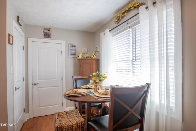 dining room featuring light wood-type flooring, a textured ceiling, and baseboards