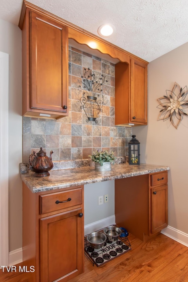 kitchen featuring tasteful backsplash, brown cabinets, a textured ceiling, and baseboards