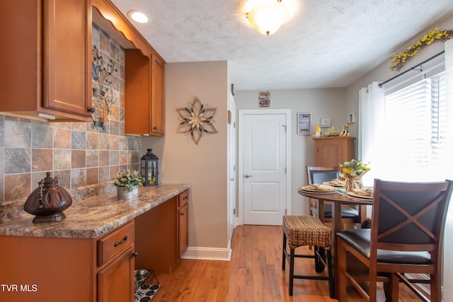 kitchen featuring a textured ceiling, light wood-style floors, baseboards, brown cabinets, and tasteful backsplash