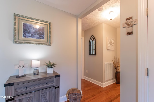corridor featuring light wood-style floors, visible vents, a textured ceiling, and baseboards