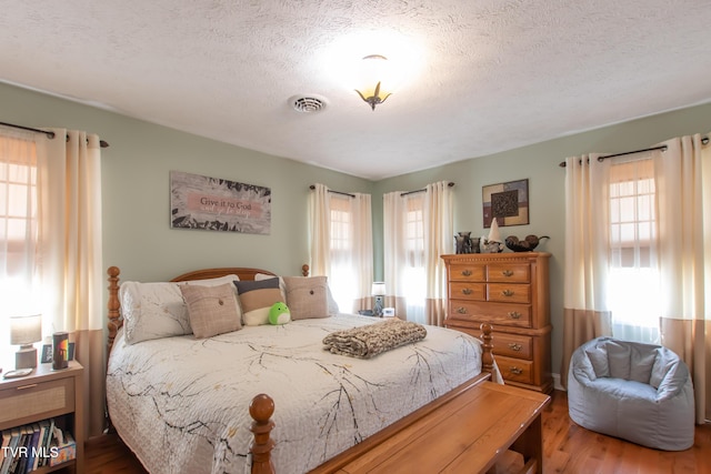 bedroom with visible vents, a textured ceiling, and wood finished floors