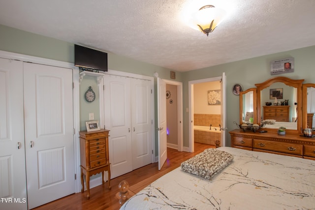 bedroom featuring multiple closets, a textured ceiling, ensuite bath, and wood finished floors