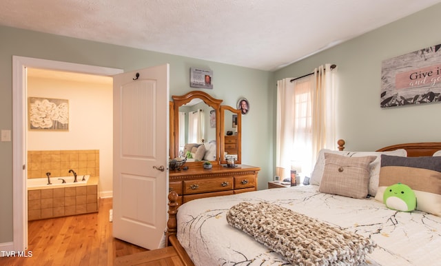 bedroom with a textured ceiling, connected bathroom, and light wood-style floors