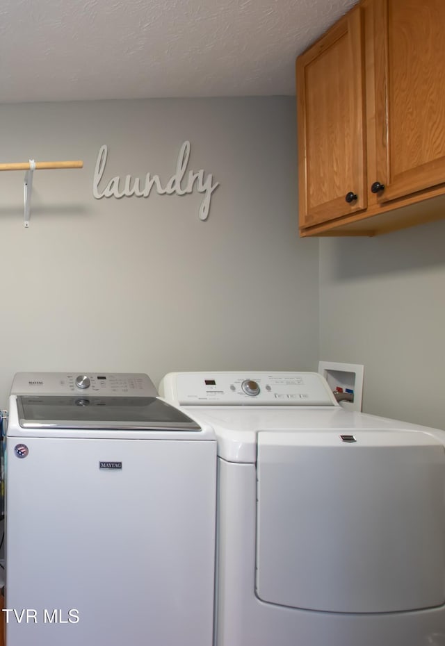 washroom with a textured ceiling, separate washer and dryer, and cabinet space