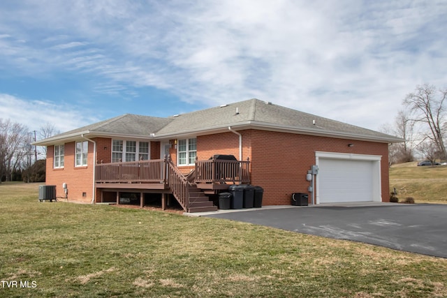 back of property featuring driveway, an attached garage, a yard, central air condition unit, and brick siding