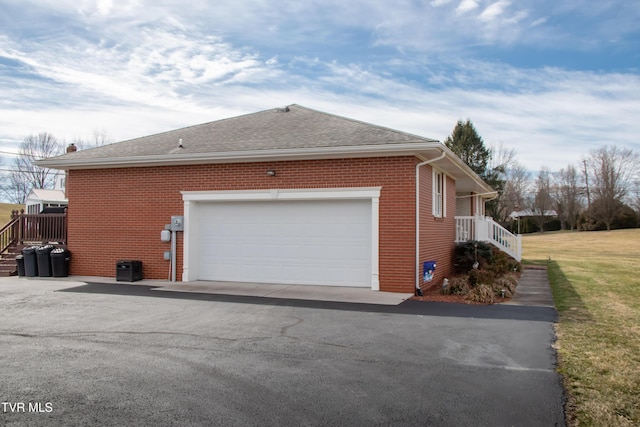 view of side of home with an attached garage, driveway, roof with shingles, and brick siding