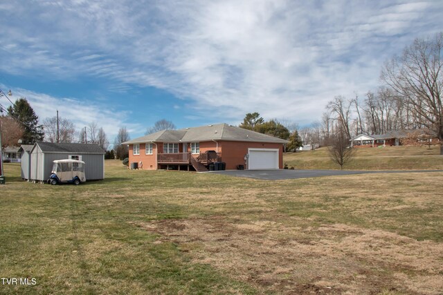 exterior space with aphalt driveway, an attached garage, an outdoor structure, a yard, and a wooden deck