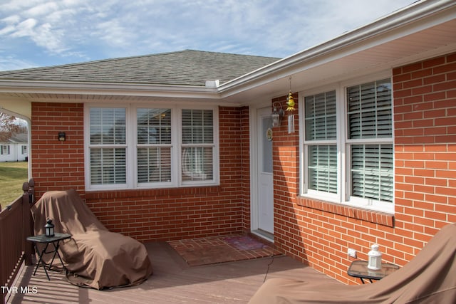 entrance to property featuring roof with shingles and brick siding