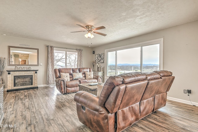 living room with a textured ceiling, a stone fireplace, and wood finished floors