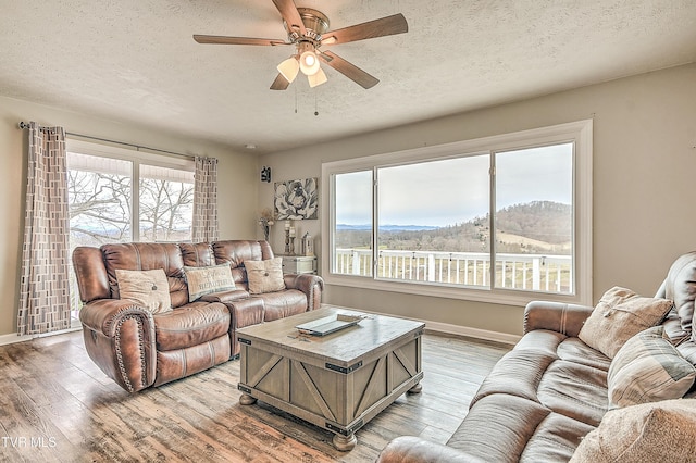 living room featuring a textured ceiling, ceiling fan, a mountain view, baseboards, and light wood finished floors