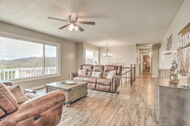 living room featuring light wood-style floors, a textured ceiling, baseboards, and ceiling fan with notable chandelier