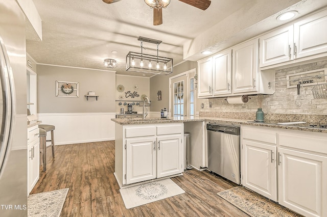 kitchen featuring dark wood finished floors, white cabinets, a peninsula, stainless steel appliances, and a sink