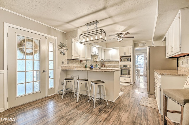 kitchen featuring stainless steel appliances, a peninsula, wood finished floors, white cabinets, and backsplash