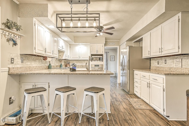 kitchen featuring stainless steel appliances, a peninsula, wood finished floors, a ceiling fan, and light stone countertops